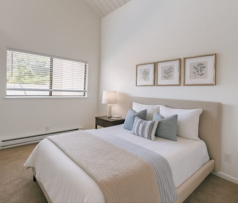 A bedroom with a large bed and a window with blinds.