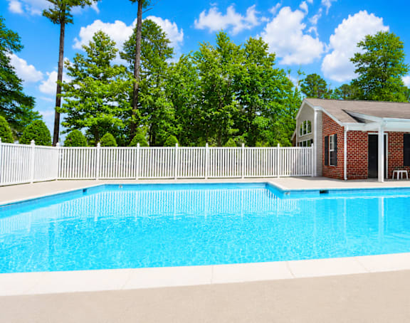 A pool in front of a house with trees in the background.