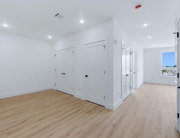 A room with white walls and wooden flooring, featuring a row of white cupboards.