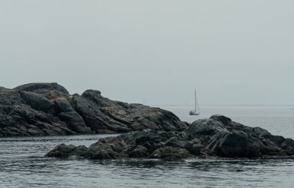 a sailboat on the water near some rocks in the ocean