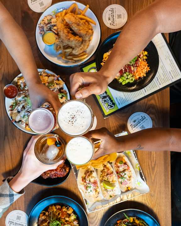A group of people toasting with beer glasses in front of a variety of dishes.