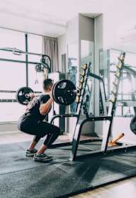 A person is squatting with a barbell in a gym.