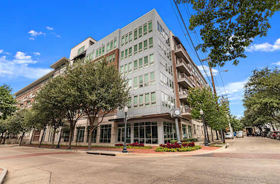 A street view of a multi-story building with a red brick sidewalk and a tree in front.