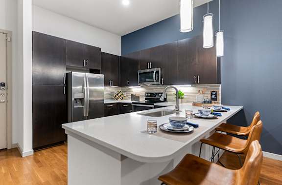 A modern kitchen with a white island and wooden chairs.