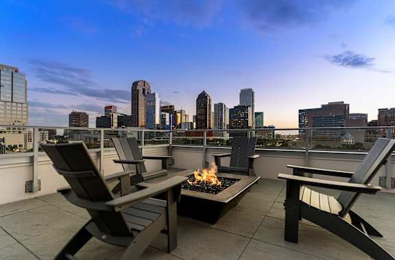 A fire pit on a patio table with two chairs and a city skyline in the background.