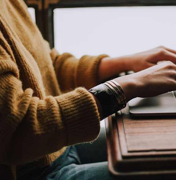 A person in a yellow sweater is typing on a laptop.
