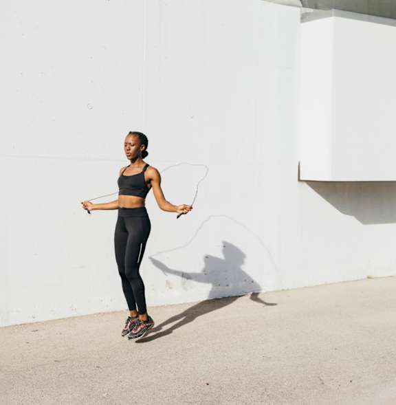 A woman in a black sports bra and leggings is standing on a concrete surface with a white wall behind her.