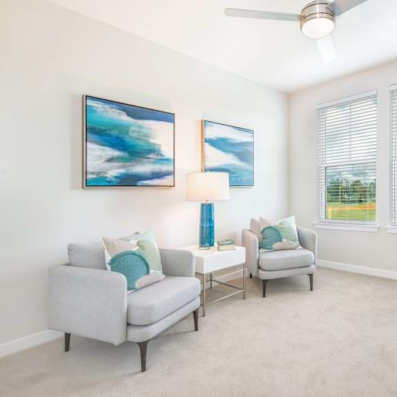 A living room with two grey couches, a ceiling fan, and two paintings on the wall.