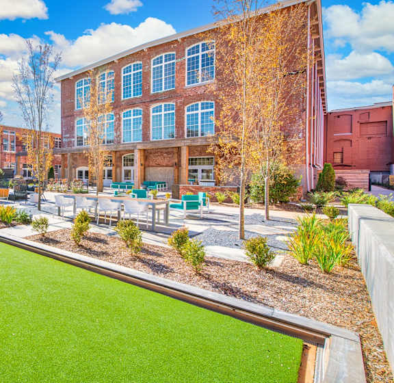 A green lawn in front of a red brick building at Judson Mill Lofts, Greenville, 29611