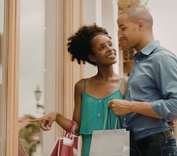 A man and woman are standing outside a store, holding shopping bags and looking at each other.