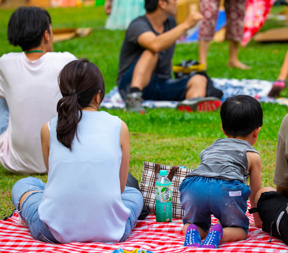 A family is sitting on a picnic blanket in a park.