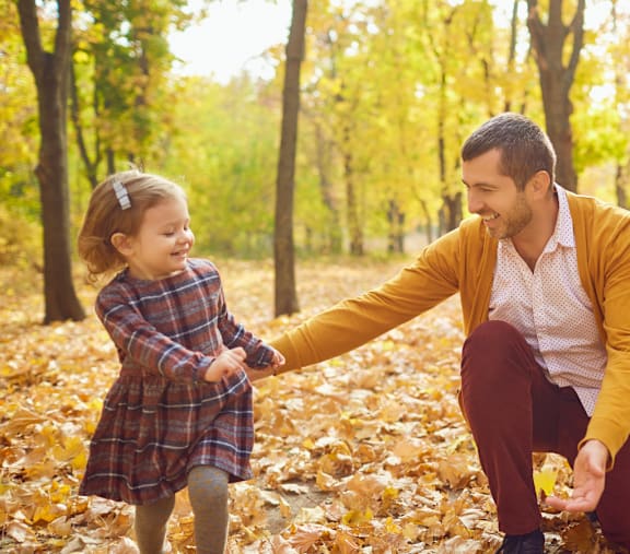 A man and a little girl are playing in a leaf-covered park.