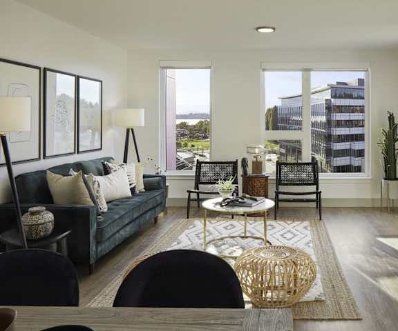 The spacious living room with a slate gray couch, black and white lamps, white throw pillows, large windows, a ceiling fan, wall art, plush chairs, coffee table, decorations, large windows, a TV, and glass doors to the balcony at Uptown at Kirkland Urban.