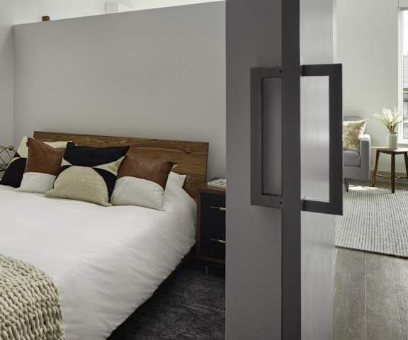 A spacious bedroom with a queen-size bed with a white, ivory, black, and brown bedspread, wall art, decorations, closet, and nightstands at Uptown at Kirkland Urban. 