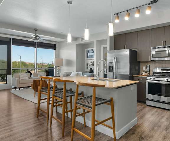 A large, modern kitchen with stainless steel appliances, kitchen utensils, marble countertops with lots of room, a kitchen island with barstools, and large dark wooden cabinets at Skywater at Tempe Town Lake Apartment Homes. 