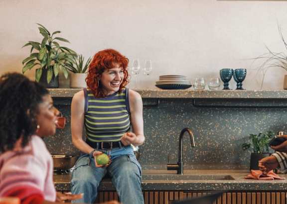 A man and woman are standing in a kitchen talking to each other.