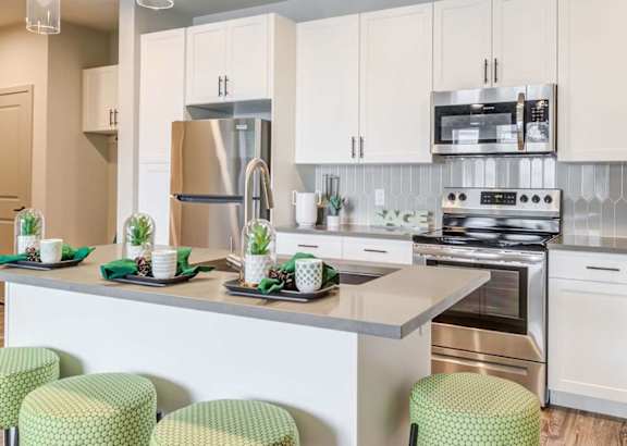 a kitchen with white cabinets and a counter with green chairs