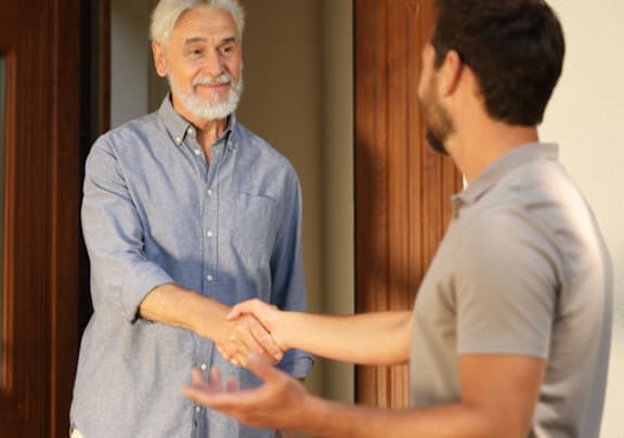 A man in a blue shirt is shaking hands with another man in a grey shirt.