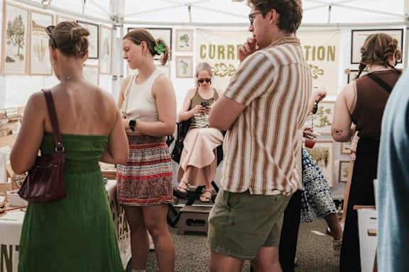 A woman in a green dress is standing in front of a table with a sign that says "CURRENT".