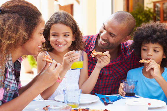 Four people eating pizza and drinking juice at a table.