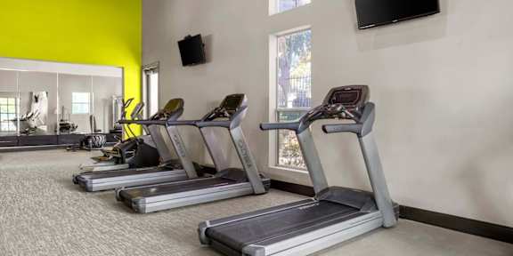 A gym with treadmills and a television mounted on the wall.