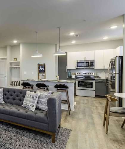 A modern living room with a grey couch, a coffee table, and a dining area in the background at Echo Park at Perry Crossing Apartments, Indiana