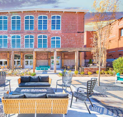 A courtyard with a wicker sofa and chairs in front of a red brick building at Judson Mill Lofts, Greenville