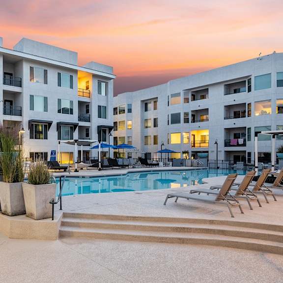 The resort-style, turquoise pool at Skywater at Tempe Towne Lake with pool chairs, umbrellas, and the apartments at Skywater at Tempe Town Lake in the background. 
