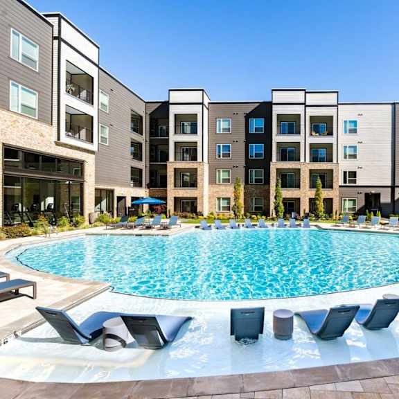 A swimming pool surrounded by lounge chairs in front of apartment buildings.
