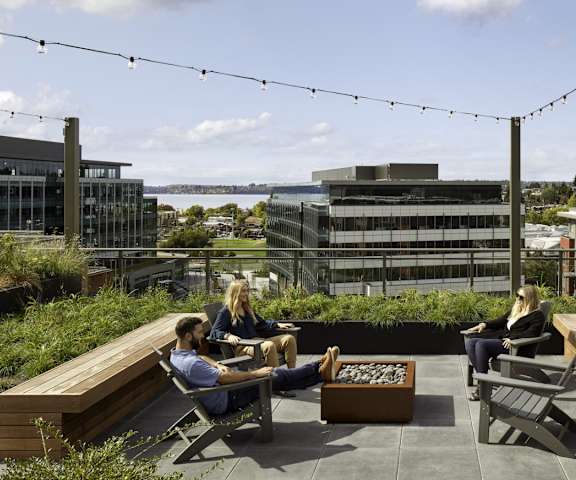Four people hanging out at the rooftop balcony lounge with couches, chairs, coffee tables, a firepit, and potted plants at Uptown at Kirkland Urban. 