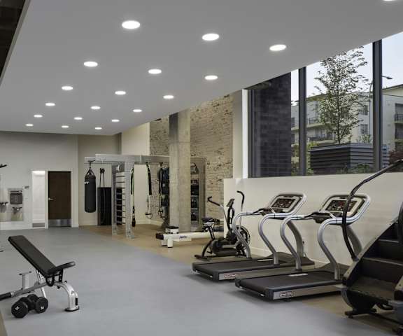 A spacious gym with cardio machines, windows, benches, TVs, and weights at Uptown at Kirkland Urban. 