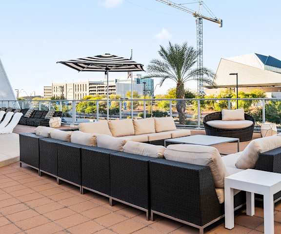 The outdoor resident patio with long black and white couches, coffee tables, large circular chairs, with tables and chairs and a view of the cityscape in the background at SKywater at Tempe Town Lake Apartment Homes. 