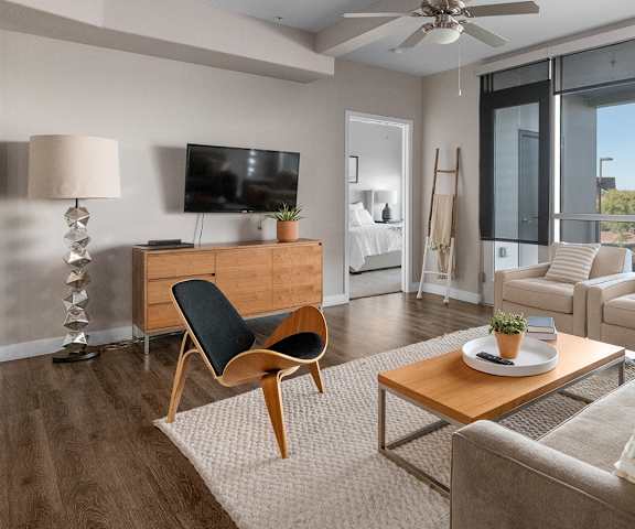 The spacious living room with a gray couch, white throw pillows, large windows, wall art, plush chair, coffee table, decorations, large windows, and a TV at Skywater at Tempe Town Lake Apartment Homes. 