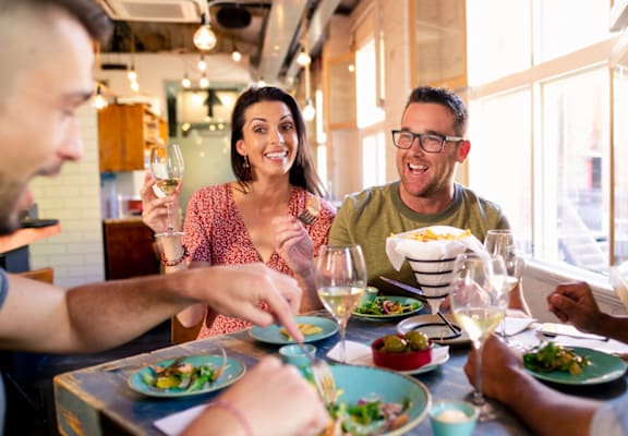 a group of people sitting around a table eating food and drinking wine