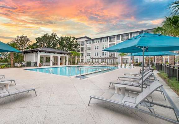 A pool area with sun loungers and umbrellas in front of a building.