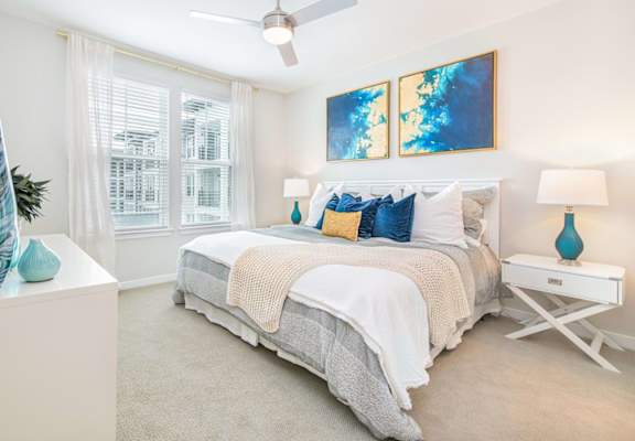A bedroom with a bed, a ceiling fan, and a painting on the wall.