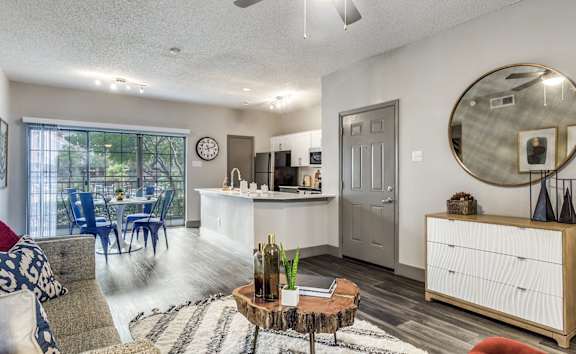 A living room with a grey couch, a wooden coffee table, and a round mirror on the wall.