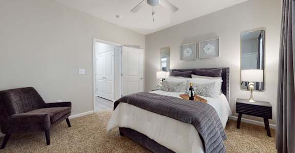 A bedroom with a bed, chair, and a ceiling fan.