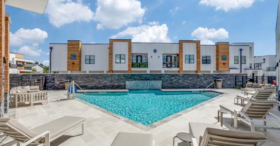 A swimming pool surrounded by lounge chairs in front of a building.
