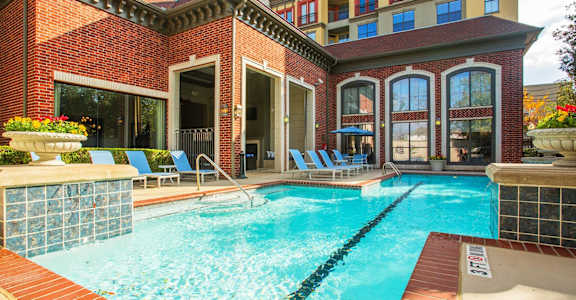A pool area with a red brick building and blue lounge chairs.