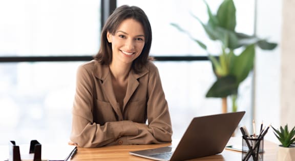 A woman in a white blouse is sitting at a desk with a laptop.