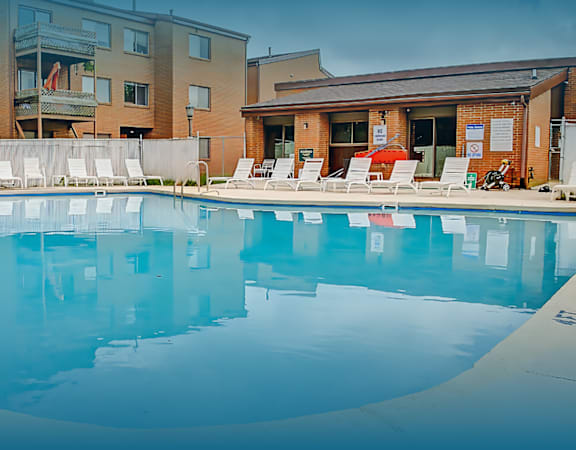 A large swimming pool with lounge chairs and apartment buildings in the background.
