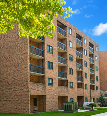 A large brick building with balconies and a tree in front.