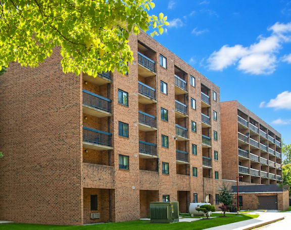 A large brick building with balconies and a tree in front.
