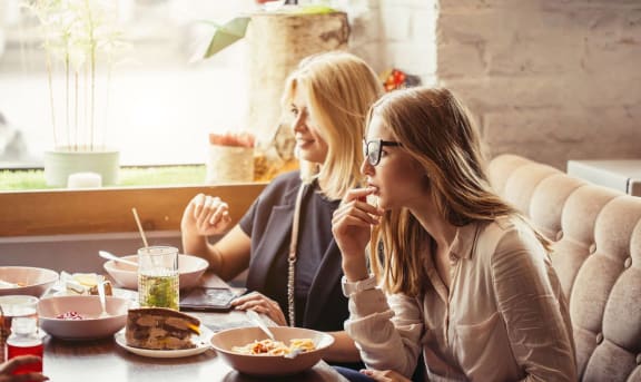 two women sitting at a table eating food in a restaurant
