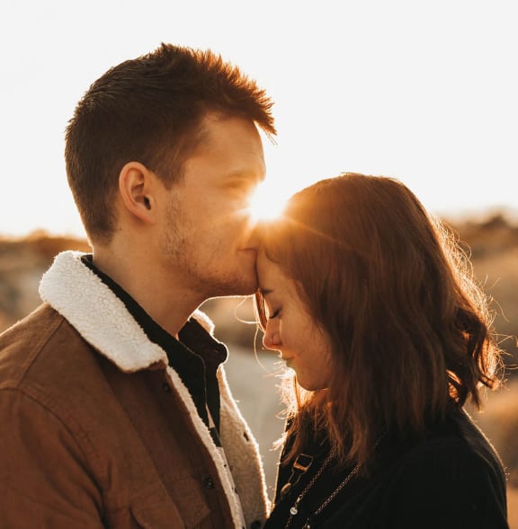 a man and woman kissing with the sun behind them