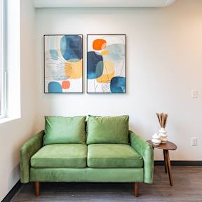 A green couch sits in front of a window with a painting on the wall.