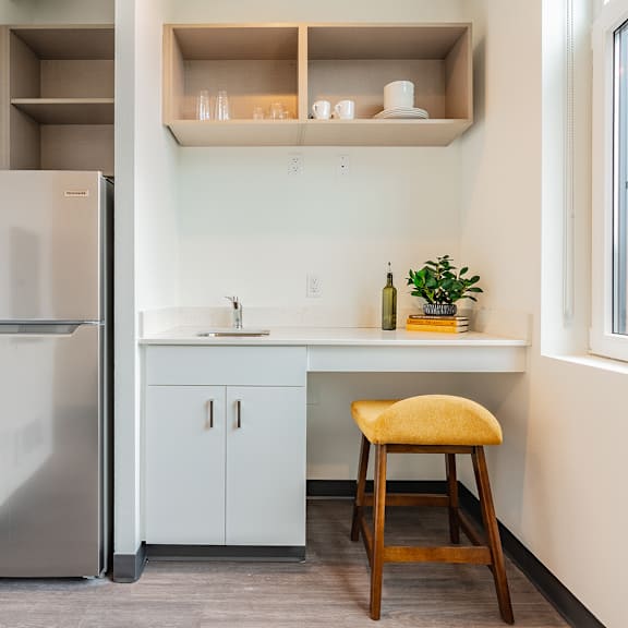 A kitchen with a stool, a fridge and a counter.