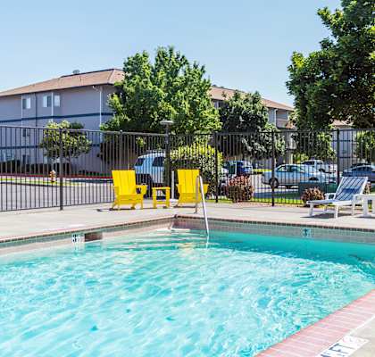 A swimming pool with yellow chairs and a black fence.