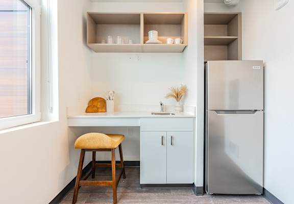 A kitchen with a stool, a fridge and a counter.